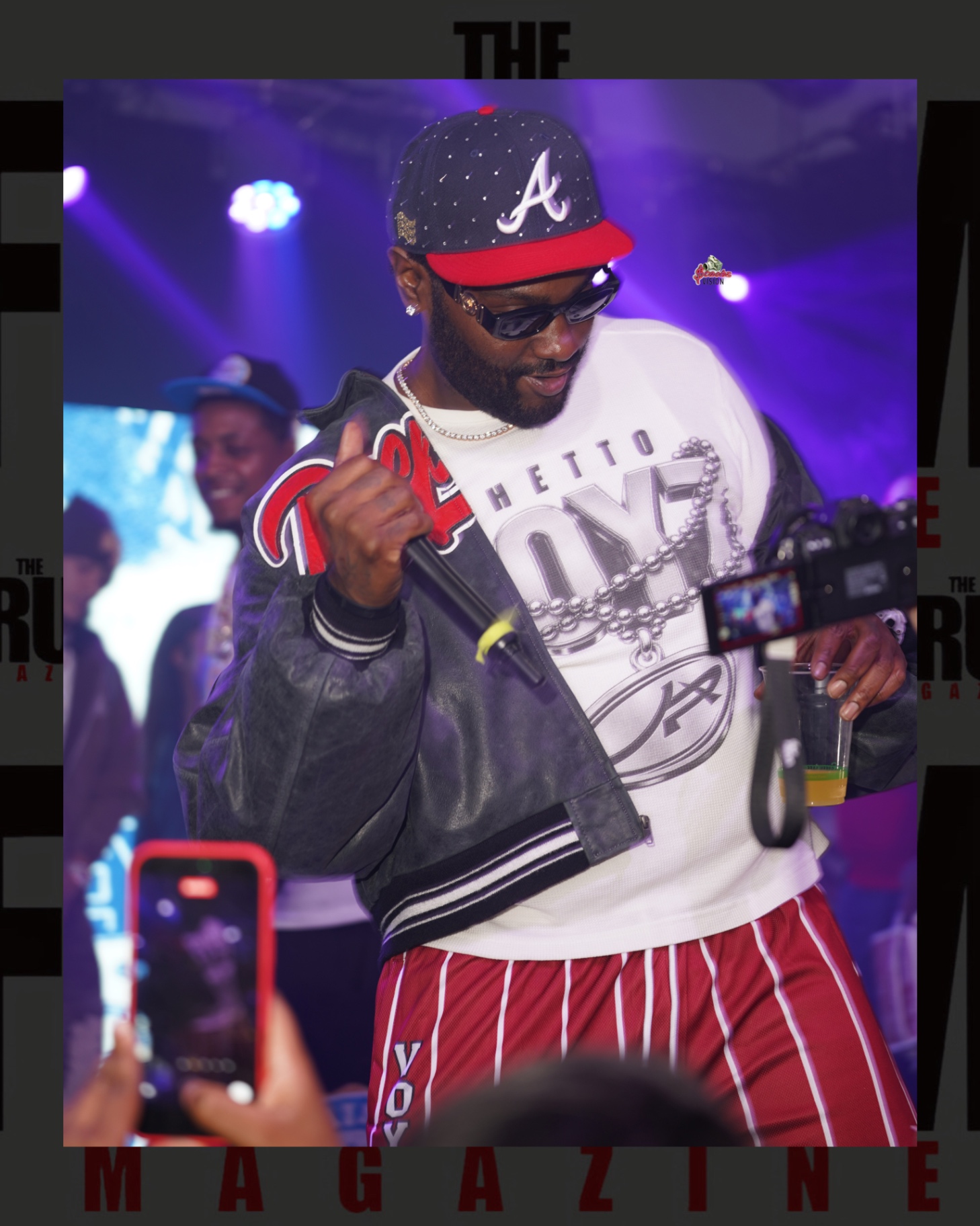 A performer in a varsity jacket and fitted cap on stage at El Club