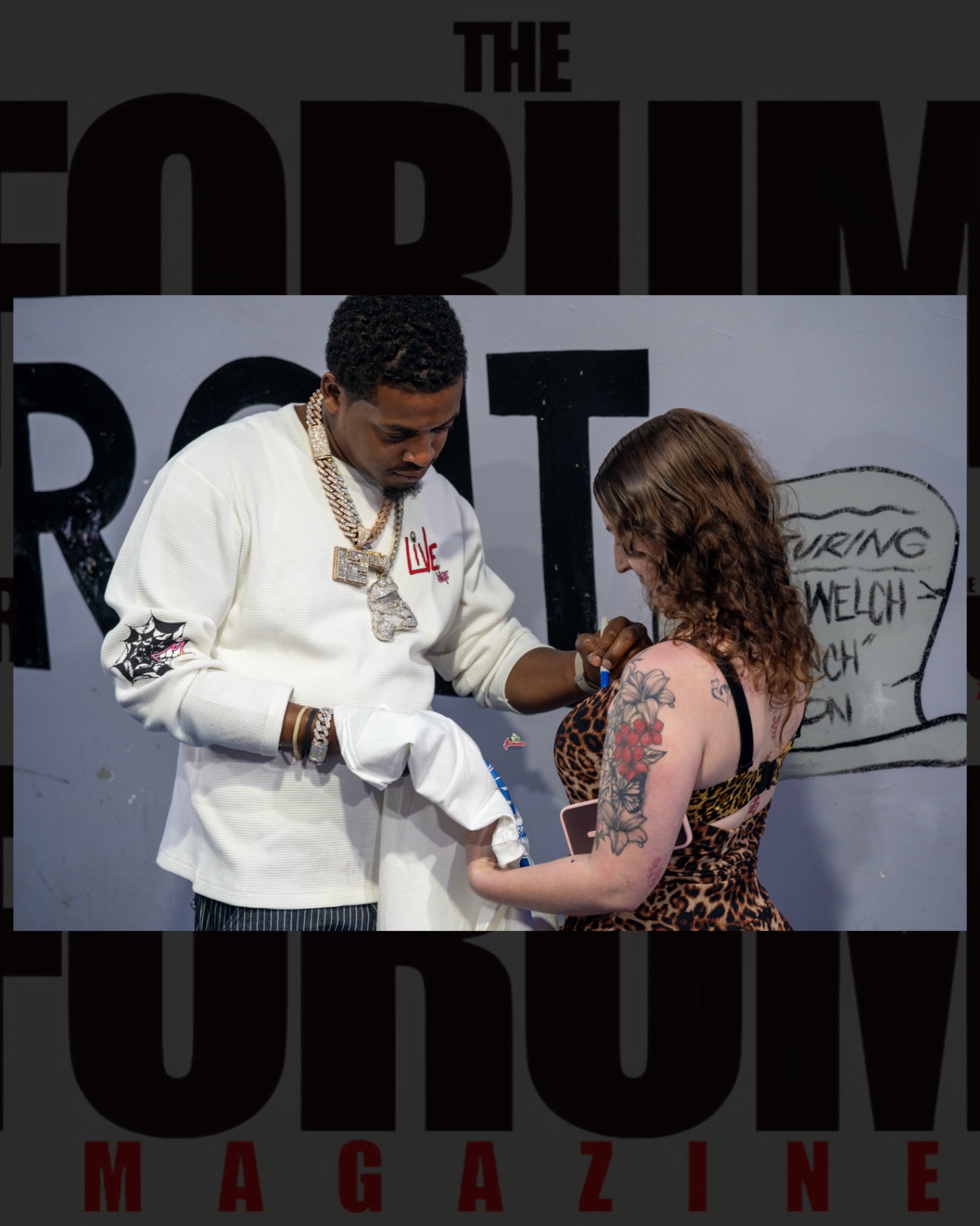 Baby Money signing an item for a fan in front of a Forum Magazine backdrop before the show