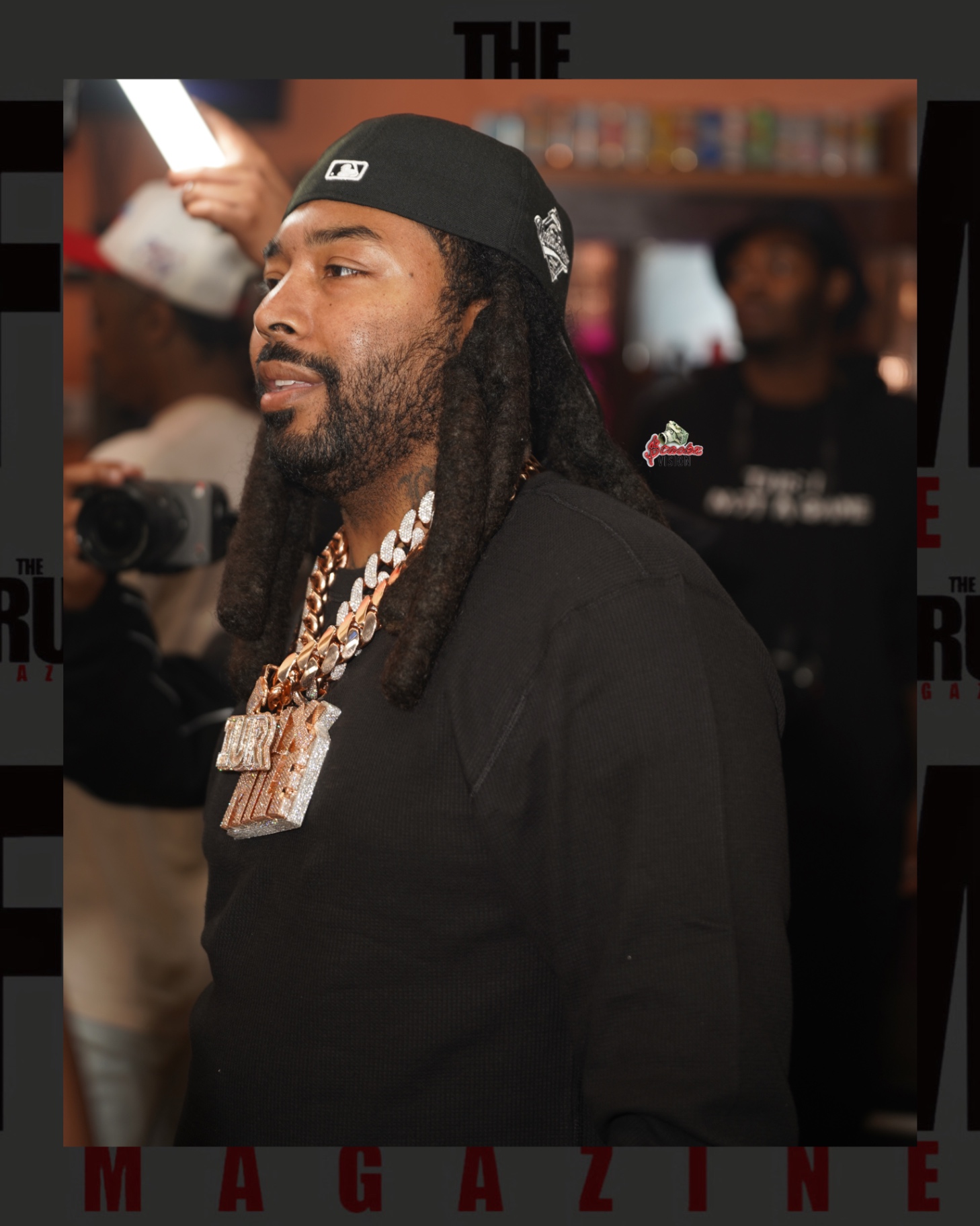 An artist in a black thermal and iced-out chain backstage at El Club